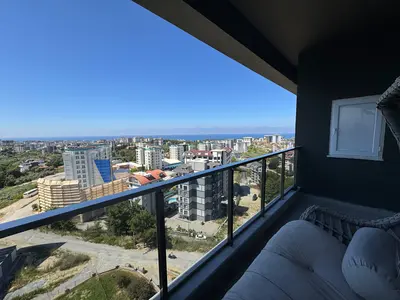 Moderni balkon s panoramskim pogledom na more i grad. Moderni balkon s prekrasnim panoramskim pogledom na more i živopisni gradski pejzaž. Sadrži elegantnu staklenu ogradu i udoban vanjski namještaj za sjedenje.