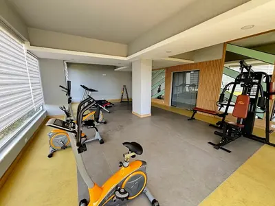 Moderna teretana u sklopu objekta s fitnes opremom. Svijetla i moderna soba za fitnes opremljena raznim spravama za vježbanje, uključujući bicikle, eliptične sprave i mašinu za utege s više stanica. Ima velike prozore sa žaluzinama i savremeni pod.