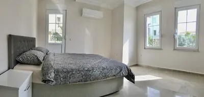 Bright Modern Bedroom with Air Conditioning and Tiled Floors. A bright and modern bedroom featuring a grey upholstered bed, shiny tiled flooring, large windows, and an air conditioning unit. Natural light fills the spacious room.