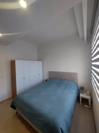 Moderna spavaća soba s ugradbenim ormarom i drvenim podom. Svijetla, moderna spavaća soba s udobnim bračnim krevetom i plavom posteljinom, svijetlim drvenim podom i velikim bijelim ugradbenim ormarom. Prirodno svjetlo prodire kroz roletne.
