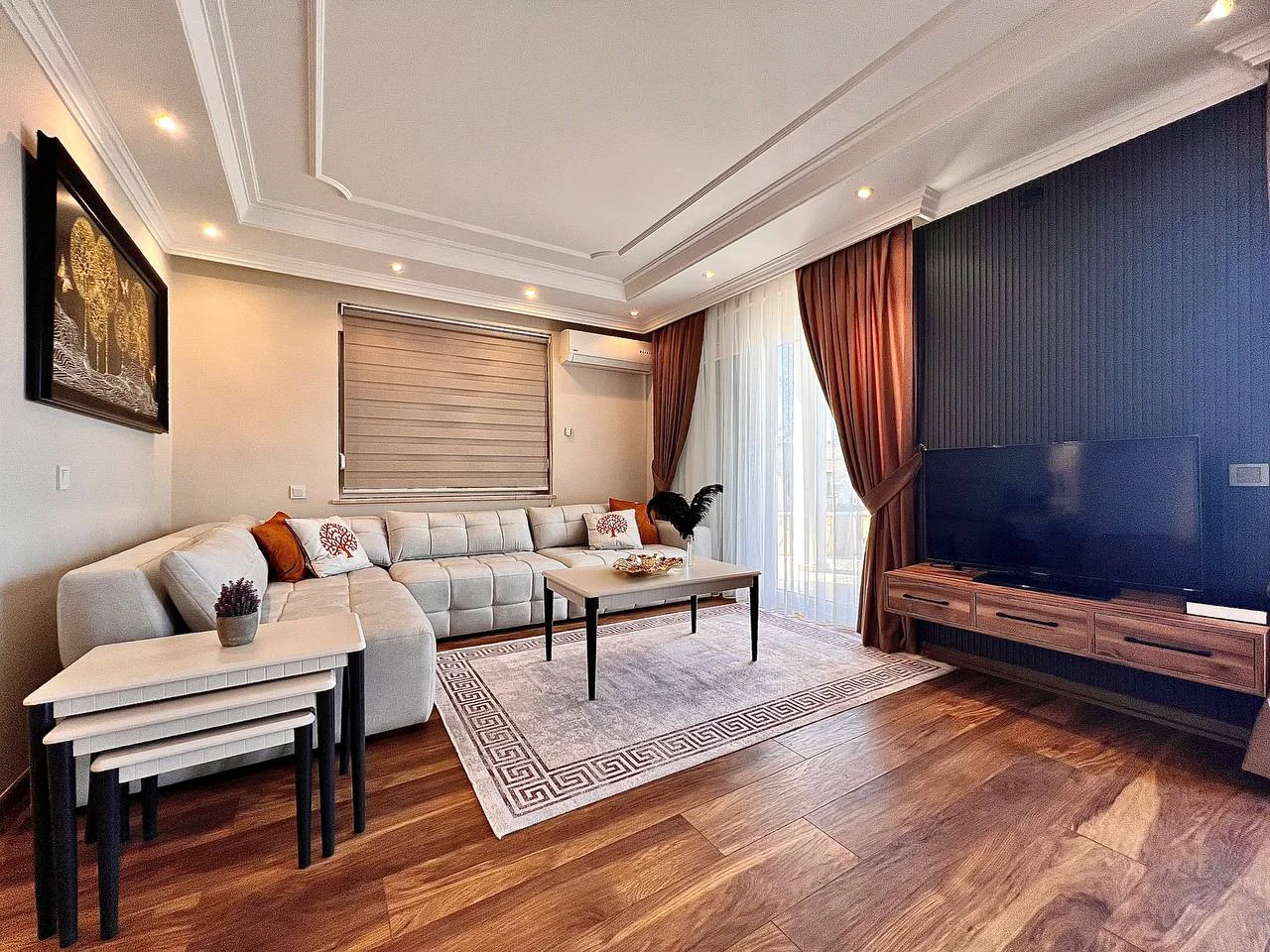 Moderan dnevni boravak sa stilskim dekorom i drvenim podom. Moderan dnevni boravak s toplim drvenim podovima, garniturom u obliku slova L, elegantnom rasvjetom i izlazom na balkon, uređen za udobnost.