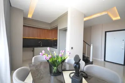 Sleek Open-Concept Kitchen and Dining Area. A sleek, modern open-concept kitchen and dining area. Features include wooden cabinets, black marble countertops, warm under-cabinet lighting, and a stylish dining table with chairs.
