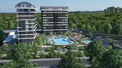 Luxury Apartment Complex with Pool and Green Amenities. Aerial view of a modern residential complex with two sleek apartment buildings, a large free-form swimming pool, water slide, playgrounds, and a sports court, surrounded by green landscaping.