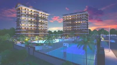 Luxury Residential Complex with Pool, Sports Courts, and Sunset View. An aerial exterior view of a modern residential complex at sunset, featuring two buildings, a large swimming pool area, a children's playground, and a multi-sport court, surrounded by palm trees.
