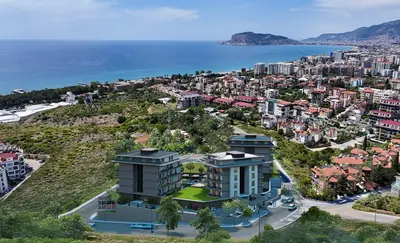 Modern Residential Complex with Panoramic Sea Views Alanya. An aerial view of a modern residential complex in Alanya, Turkey, featuring multiple apartment buildings with green landscaping and stunning panoramic Mediterranean Sea and city views.