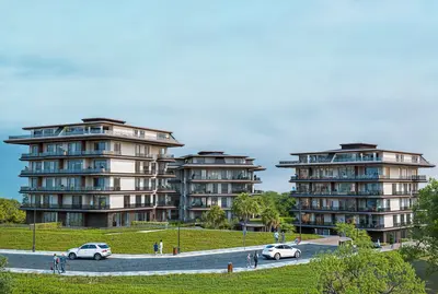Modern Residential Buildings within a Lush Green Landscape. Exterior view of a modern residential complex featuring contemporary multi-story apartment buildings with large balconies. Lush green landscaping and a winding road provide a serene environment.