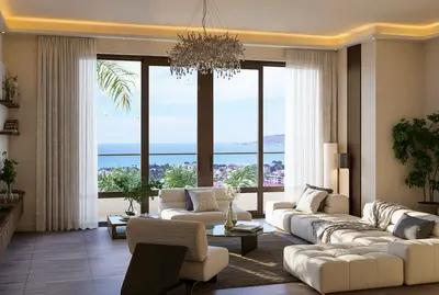 Modern Living Room with Panoramic Sea and City View. A bright, modern living room with large windows offering a panoramic sea and city view. Features include light modular sofas, a glass coffee table, a sparkling chandelier, and elegant cove lighting.