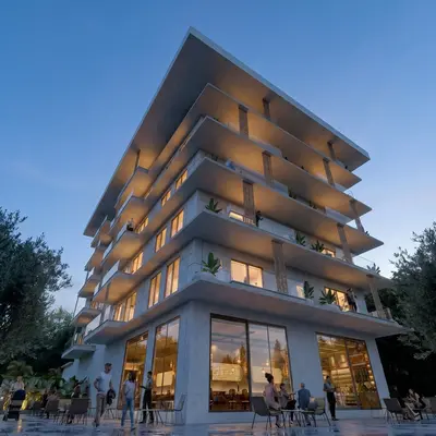 Modern Apartment Building with Balconies and Commercial Space. Exterior view of a modern multi-story apartment building with wide balconies, glass railings, and illuminated windows at dusk. The ground floor features a commercial area with outdoor seating.