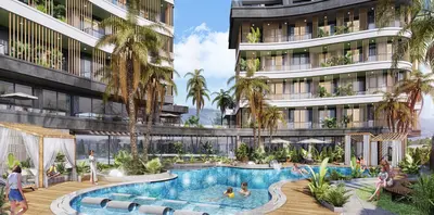 Modern Apartment Complex with Large Outdoor Pool Area. An inviting resort-style outdoor pool area with a large free-form swimming pool, wooden decks, sunbeds, and lush palm trees. Modern residential buildings are visible in the background.
