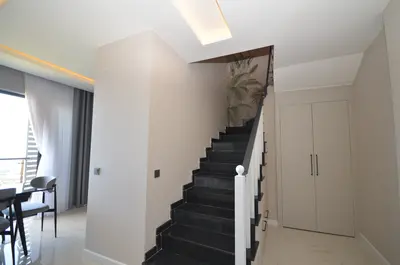 Modern Interior with Elegant Staircase and Dining Area. A modern interior features an elegant dark staircase with white railing, tropical wallpaper, and a dining area by a large window. Includes built-in storage.