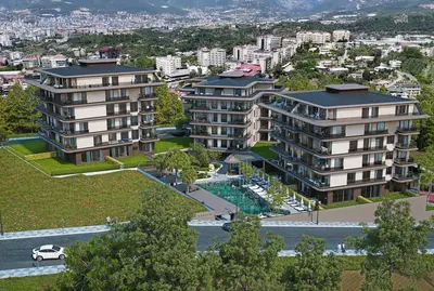 Modern Residential Complex with Pool and Mountain Views. Aerial view of a modern residential complex with multiple apartment buildings, a large outdoor swimming pool, and green landscaped areas. A paved road and distant city with mountains are visible.