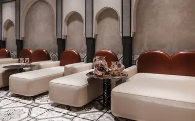 Elegant Spa Relaxation Zone with Arched Nooks. Sophisticated spa relaxation area with arched alcoves and intricate patterned floor tiles. Plush lounge chairs, modern side tables, and refreshing fruit-infused water create a luxurious, serene ambiance.