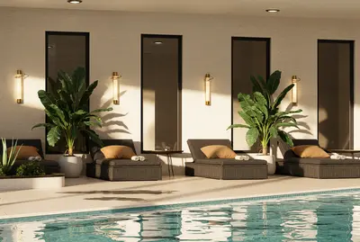 Luxurious Indoor Pool Area with Modern Sun Loungers. A modern indoor swimming pool area featuring dark sun loungers with cushions and towels. Potted green plants and stylish wall sconces adorn the bright, contemporary space, offering a relaxing amenity.