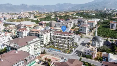 Modern Residential Complex with Pool and Mountain Backdrop. An aerial view of a modern multi-story residential building, featuring an outdoor swimming pool, set within a vibrant Turkish city against a mountainous landscape.