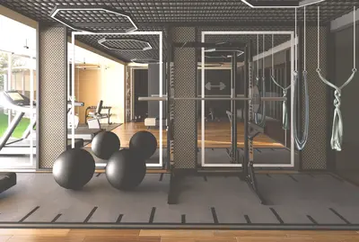 Modern Fully Equipped Fitness Center and Gym Space. A modern, fully equipped gym with a squat rack, exercise balls, and aerial yoga hammocks. The vibrant space features wood and rubber flooring, contemporary hexagonal lighting, and large mirrors.