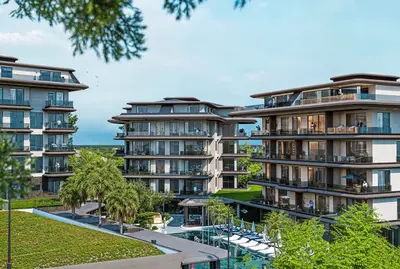 Modern Luxury Apartment Complex with Resort-Style Pool. Exterior view of a modern, upscale residential complex featuring multiple buildings with large balconies, a resort-style swimming pool, and lush green landscaping.