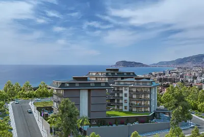 Luxury Hillside Apartments with Panoramic Sea and City View. Exterior view of a modern apartment complex on a hillside, featuring lush green landscaping and stunning panoramic views of the sea and city skyline.