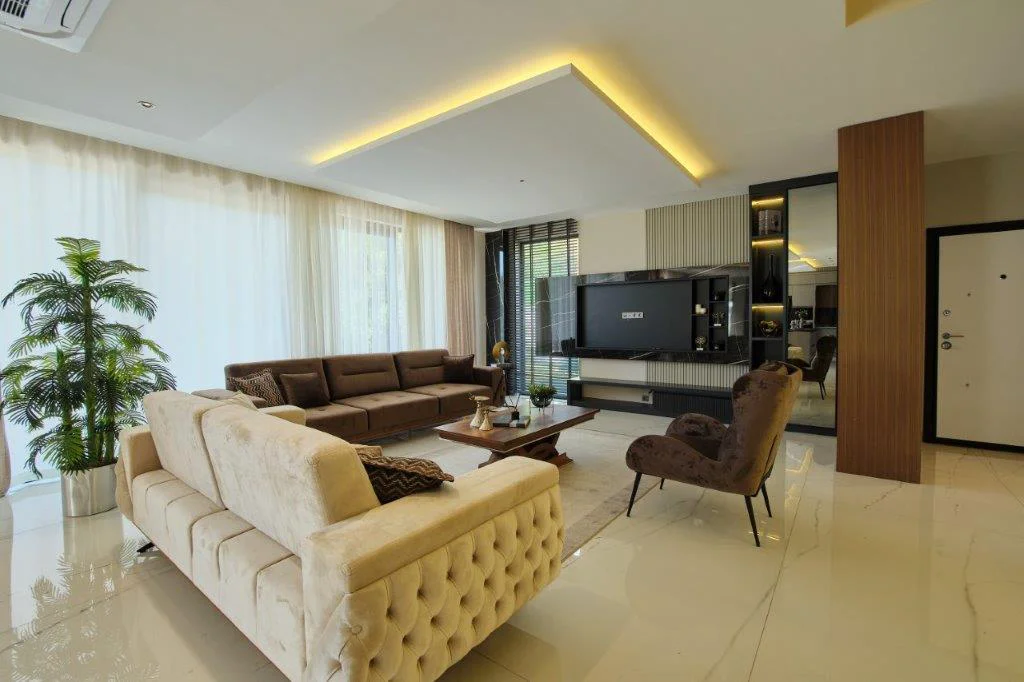 Rummelig moderne stue med elegant design og tv-møbel. Rummelig moderne stue med elegante beige og brune sofaer, et stort væghængt tv-møbel og lyst klinkegulv. Skjult belysning og tynde gardiner fuldender det sofistikerede look.