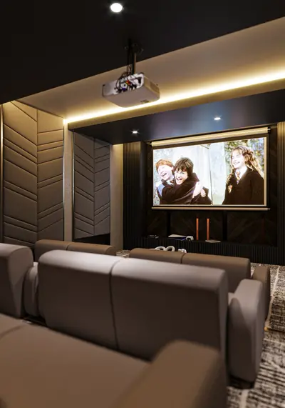 Luxury Home Cinema Room with Projector and Comfortable Seating. A modern, luxurious home cinema room featuring a large projector screen, tiered comfortable brown seating, stylish patterned wall panels, and ambient lighting. Perfect for entertainment.