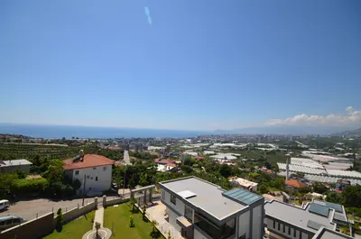 Stunning Panoramic Sea and City View from Elevated Property. An expansive panoramic view from a property's high vantage point, showcasing the blue Mediterranean Sea, a sprawling city, and lush green landscapes with greenhouses under a clear sky.