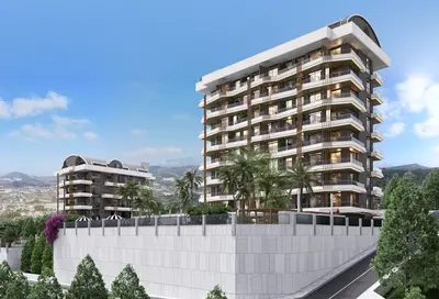 Moderni stambeni kompleks s balkonima i pogledom na planine. Vanjski pogled na dvije moderne stambene zgrade. Višespratnice s balkonima i staklenim ogradama. Sadrži bujne palme, zeleno uređenje i udaljene planine pod vedrim plavim nebom.