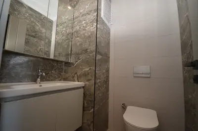 Modern Bathroom with Elegant Marble Vanity and Toilet. A modern bathroom featuring a white wall-mounted vanity with sink and mirror. Elegant grey marble accent walls complement the light-colored tiled walls, alongside a contemporary wall-hung toilet.