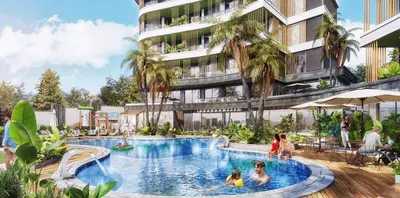 Stunning Residential Complex with Resort-Style Pool. The resort-style swimming pool area of a modern residential complex. It includes a large blue pool, wooden deck with sun loungers, outdoor dining, and abundant tropical landscaping around the contemporary building.