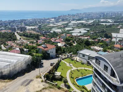 Panoramic Sea and City View from Luxury Residence. This outdoor view showcases a modern residential complex featuring a swimming pool and landscaped gardens. It offers a stunning panoramic vista of the Mediterranean Sea and a vibrant coastal city.