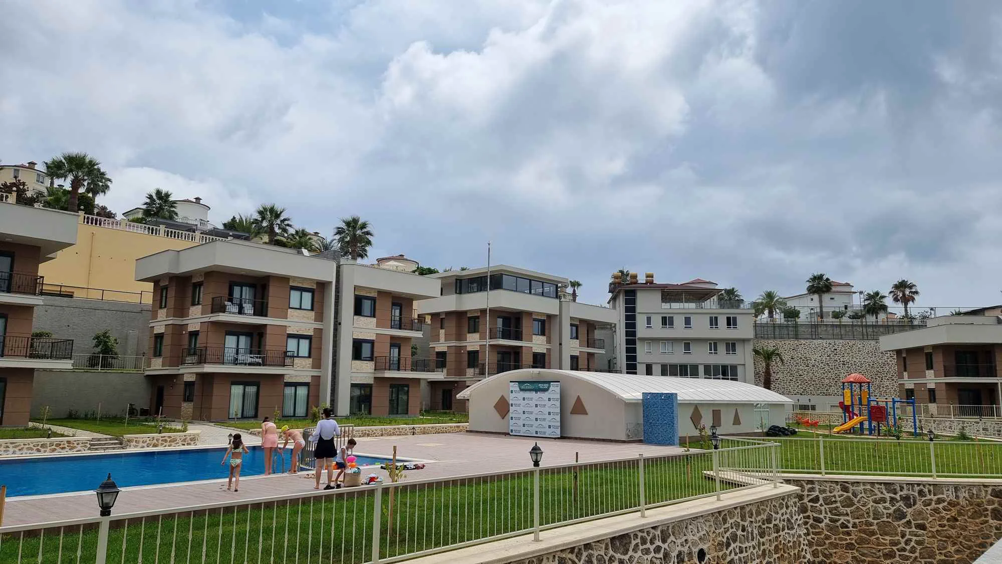 Moderni apartmani s bazenom i igralištem u Turskoj. Eksterijer modernog stambenog kompleksa u Turskoj. Sadrži više stambenih zgrada, veliki bazen, zeleni travnjak i živopisno dječje igralište, nudeći izvrsne sadržaje na otvorenom.