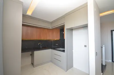 Sleek Modern Kitchen with Marble Backsplash and Wood Cabinets. A modern, well-lit kitchen featuring light beige tiled flooring, grey base cabinets, and warm wooden upper cabinets. It has a striking black marble backsplash with under-cabinet lighting and a golden faucet.