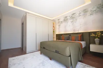 Elegant Bedroom with Nature-Inspired Mural and Modern Wardrobe. This modern bedroom features an elegant green bed, a stylish nature-inspired wall mural, and built-in wardrobe storage. Ambient lighting enhances the room's warm and sophisticated atmosphere.