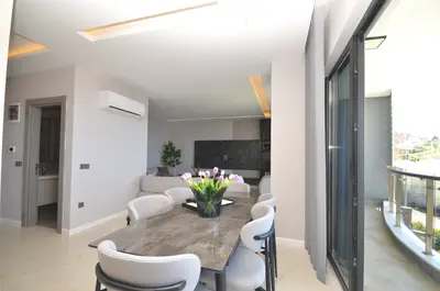 Modern Open-Plan Living Dining Room with Balcony. Modern open-plan living and dining room with sleek tiled floors and stylish furniture. Features air conditioning and a large sliding door opening to a private balcony with glass railings.