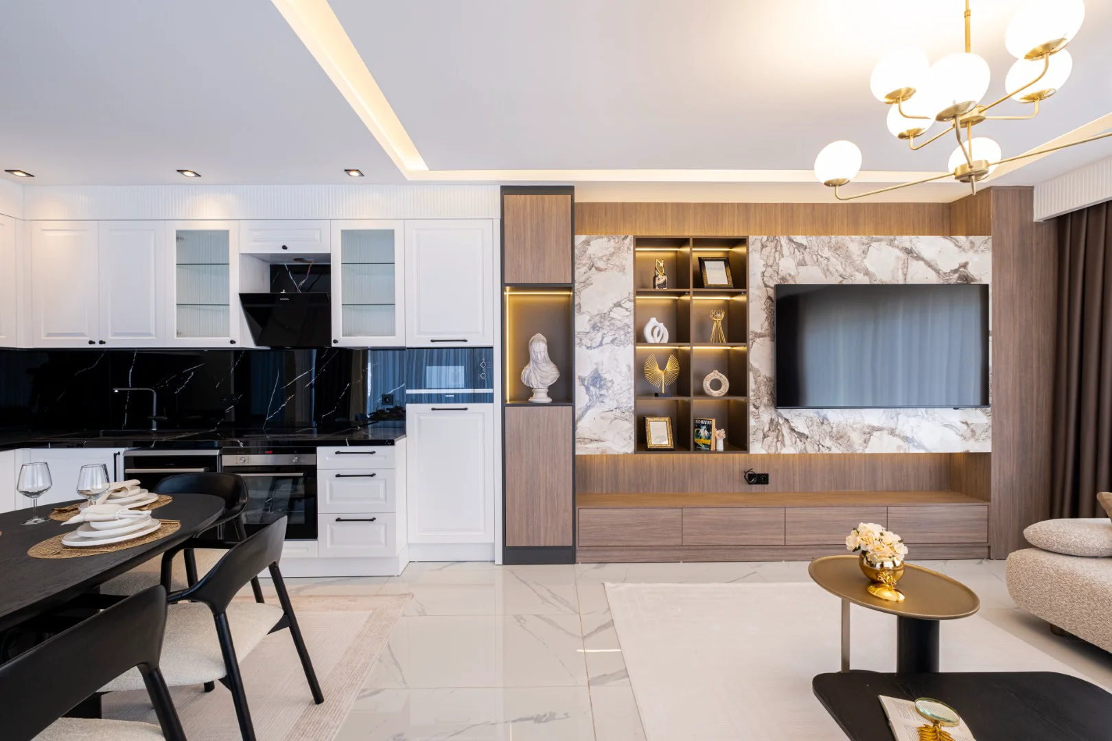Modern Open-Plan Living Room and Kitchen with Marble Accents. A modern open-plan living room and kitchen with white cabinets, black marble countertops, and an integrated entertainment unit. Features polished tile flooring and contemporary lighting.