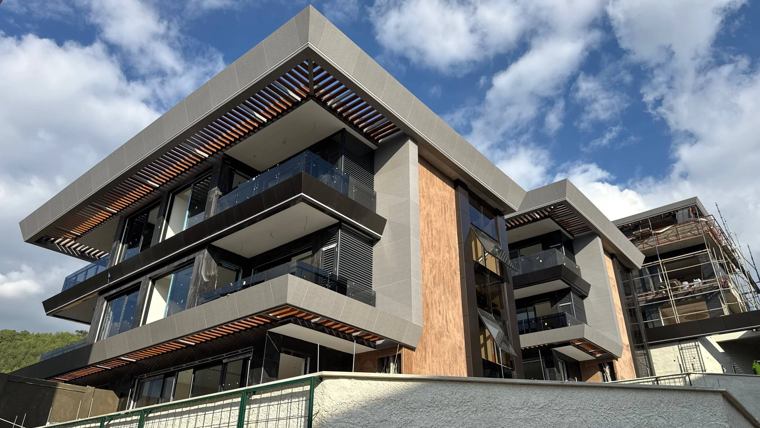 Moderni apartmanski objekat sa balkonima. Pogled na moderan, višespratni apartmanski objekat pod oblačnim nebom, sa elegantnim sivim i drvenim oblogama, velikim prozorima i balkonima sa savremenim staklenim ogradama.