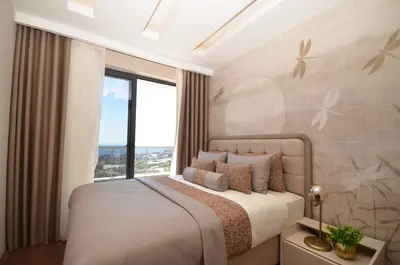 Stylish Modern Bedroom with Panoramic City and Sea View. A stylish, modern bedroom featuring a comfortable bed, unique dragonfly wallpaper, and a floor-to-ceiling window with panoramic city and sea views. Well-appointed with elegant curtains and lighting.