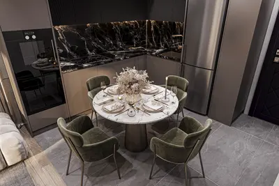Modern Kitchen Dining Area with Elegant Black Marble Accents. A modern, renovated kitchen dining area featuring black marble countertops, sleek stainless steel appliances, and a round marble-patterned dining table with four green velvet chairs.