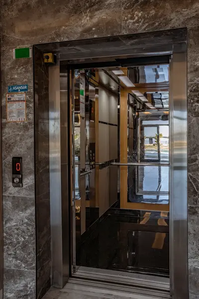 Modern Elevator with Panoramic Coastal View. This modern elevator features sleek stainless steel and dark polished surfaces. Through its open doors, a beautiful panoramic view of the sea and coastline is revealed.