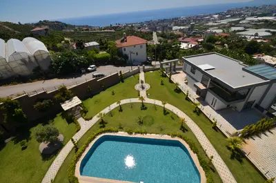 Expansive Modern Property with Private Pool and Sea View. Aerial view of a modern luxury villa exterior featuring a large swimming pool, meticulously landscaped garden with winding paths, and a stunning panoramic sea view.