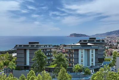 Modern Coastal Apartments with Panoramic Sea and City Views. Exterior view of a modern residential complex featuring multiple buildings with balconies and green landscaping. It offers panoramic views of the vast blue sea, a coastal city, and distant mountains.
