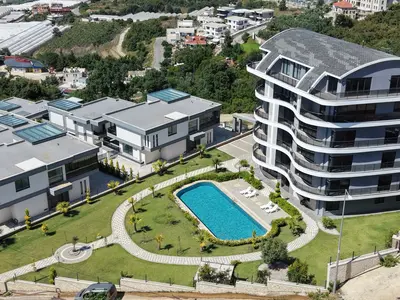 Modern Residential Complex with Outdoor Pool and Villas. Aerial view of a modern residential complex. Features a vibrant outdoor swimming pool, sun loungers, and landscaped gardens surrounding contemporary villas and an apartment building.