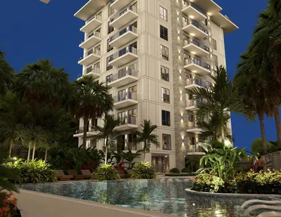 Modern Residential Building with Illuminated Pool and Garden. Exterior view of a modern apartment building at night. Features a large, illuminated swimming pool with lounge chairs, surrounded by lush tropical gardens and palm trees, offering a luxurious ambiance.