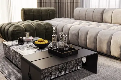 Luxurious Modern Living Room with Designer Sofas and Unique Coffee Tables. A luxurious modern living room featuring a green and grey sectional sofa, two unique coffee tables with marble and black accents, crystal decanters, and a patterned rug.