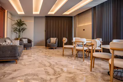 Modern Spacious Lobby with Elegant Marble Floors. Spacious, modern lobby area featuring elegant marble floors and contemporary recessed ceiling lighting. Includes comfortable grey sofa, armchairs, stylish round tables with cream chairs, and a large indoor plant.