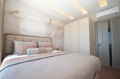 Stylish Modern Bedroom with Unique Wall Mural and Built-in Wardrobe. A modern and elegant bedroom featuring a large bed with a cushioned headboard, unique dragonfly wall mural, recessed ceiling lights, and built-in wardrobes. Includes air conditioning and wooden flooring.