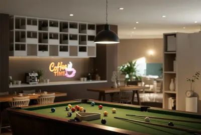 Modern Game Room with Pool Table and Coffee Bar. A modern, well-lit social area featuring a green felt pool table. An inviting coffee bar with a neon 'Coffee Time' sign and sleek shelving is visible in the background.