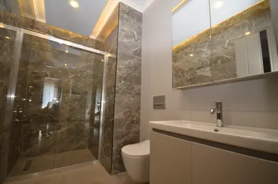 Contemporary Bathroom with Elegant Marble Shower and Vanity. This contemporary bathroom boasts a glass-enclosed shower with luxurious dark marble-patterned walls. It also features a sleek vanity, mirror cabinet, and recessed lighting.