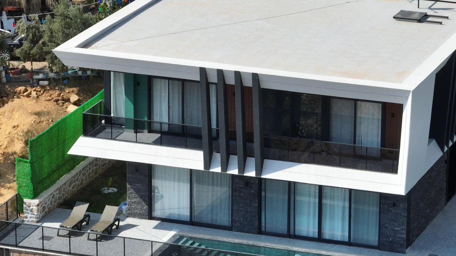 Moderne Villen-Außenansicht mit Balkon und privatem Pool. Moderne Villen-Außenansicht mit elegantem Design, großen Glastüren, einem Balkon und einer Terrasse mit Sonnenliegen an einem privaten Pool.