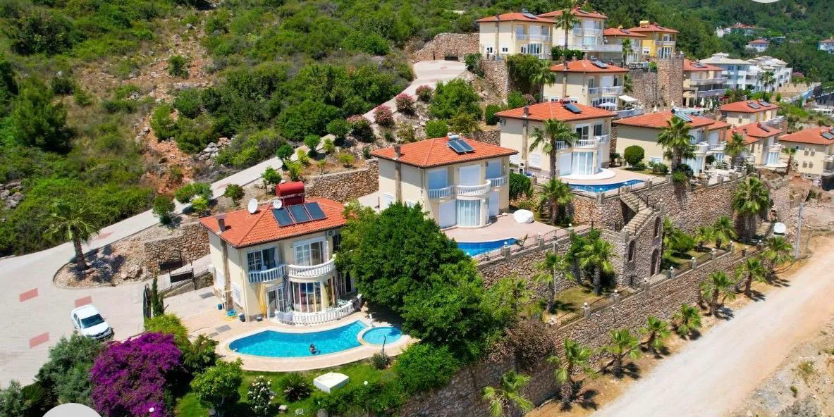 Luxuriöse Hangvillen mit privaten Pools und grüner Umgebung. Eine Luftaufnahme einer modernen Wohnanlage mit mehreren zweistöckigen Villen, jede mit privatem Pool und Sonnenkollektoren, eingebettet in einen terrassierten grünen Hang.