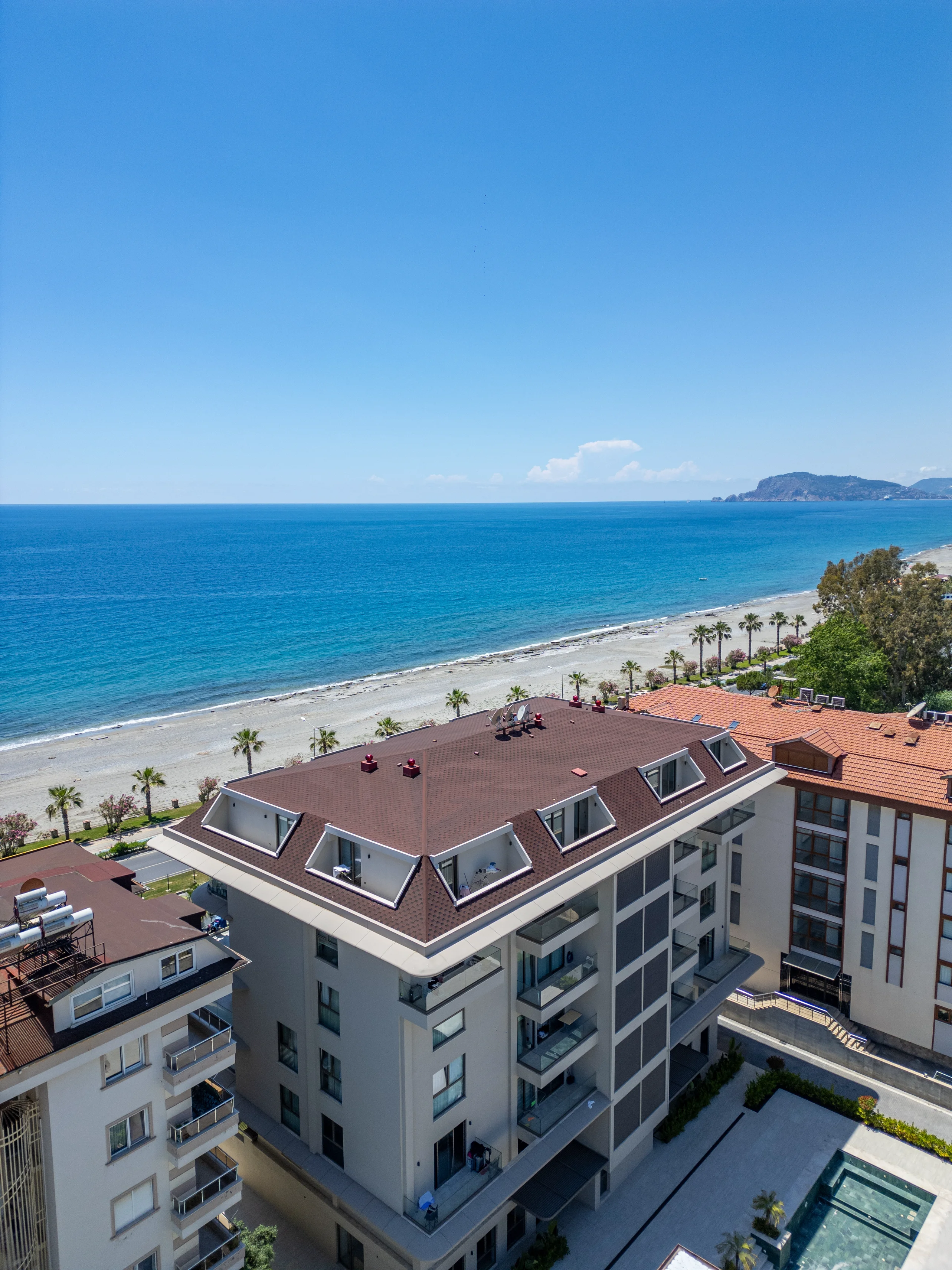 Atemberaubende Küstenapartments mit direktem Strandzugang und Meerblick. Eine Luftaufnahme eines modernen Apartmentkomplexes direkt an einem Sandstrand mit atemberaubendem Blick auf das Mittelmeer. Mit klarem blauem Himmel und einem Außenpool.