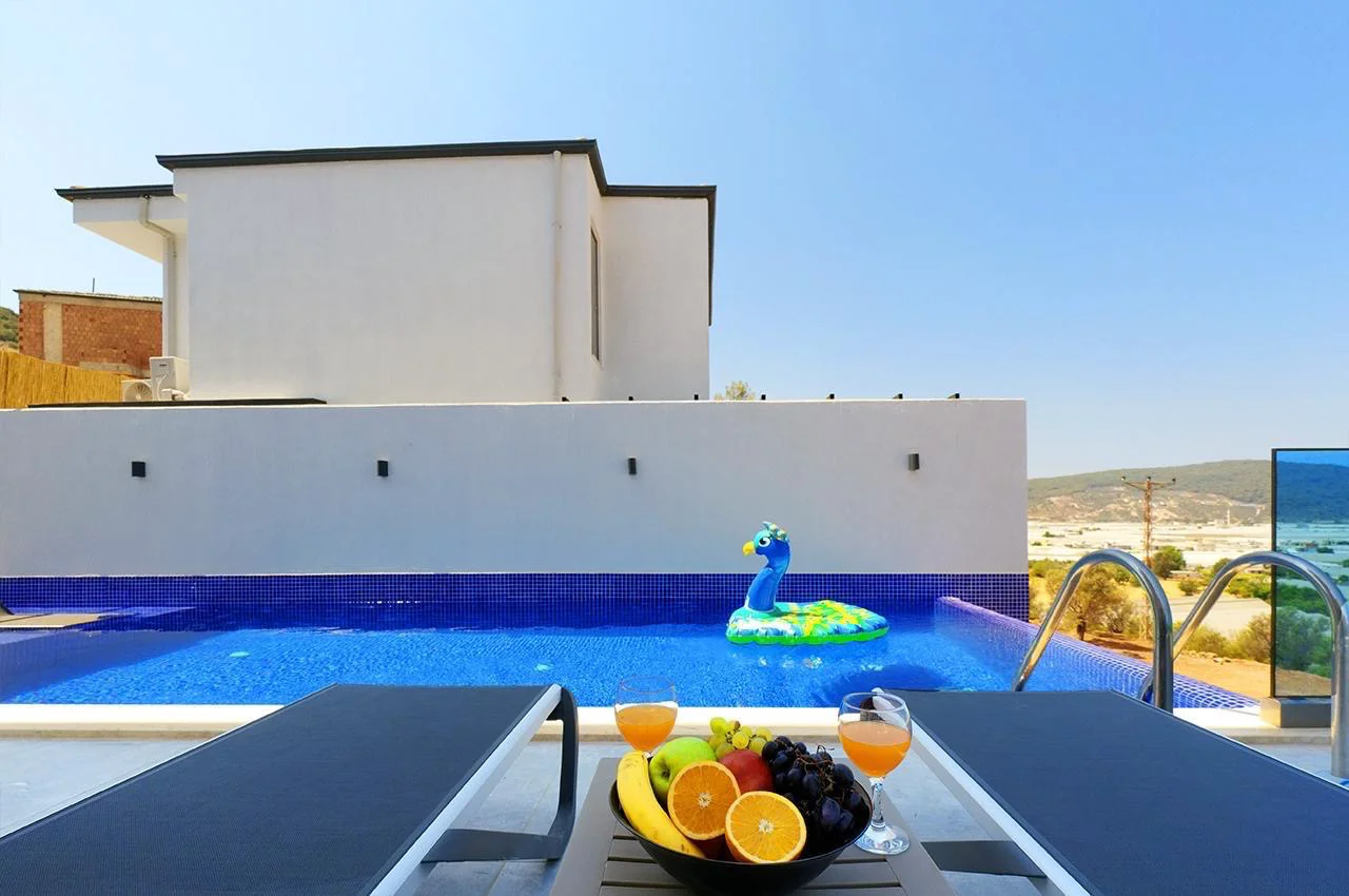 Luxuriöser Privatpool mit wunderschönem Bergblick. Ein einladender, moderner Außenpoolbereich mit einem hellblau gefliesten Swimmingpool, zwei Liegestühlen und einem Tisch mit frischem Obst und Saft. Mit einem wunderschönen Blick auf Berge und Täler unter klarem Himmel.